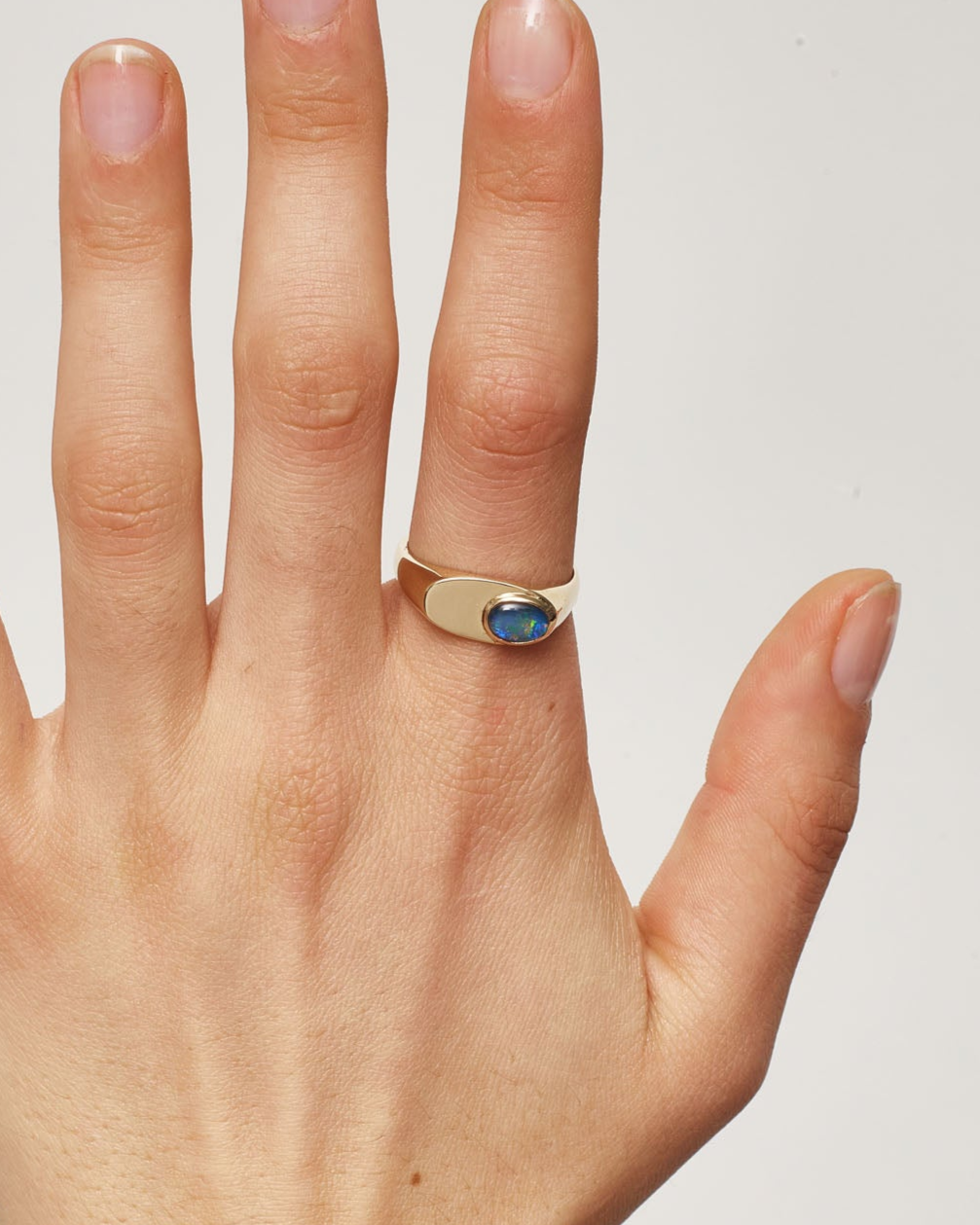 Hand wearing a gold ring with a blue stone on a plain background