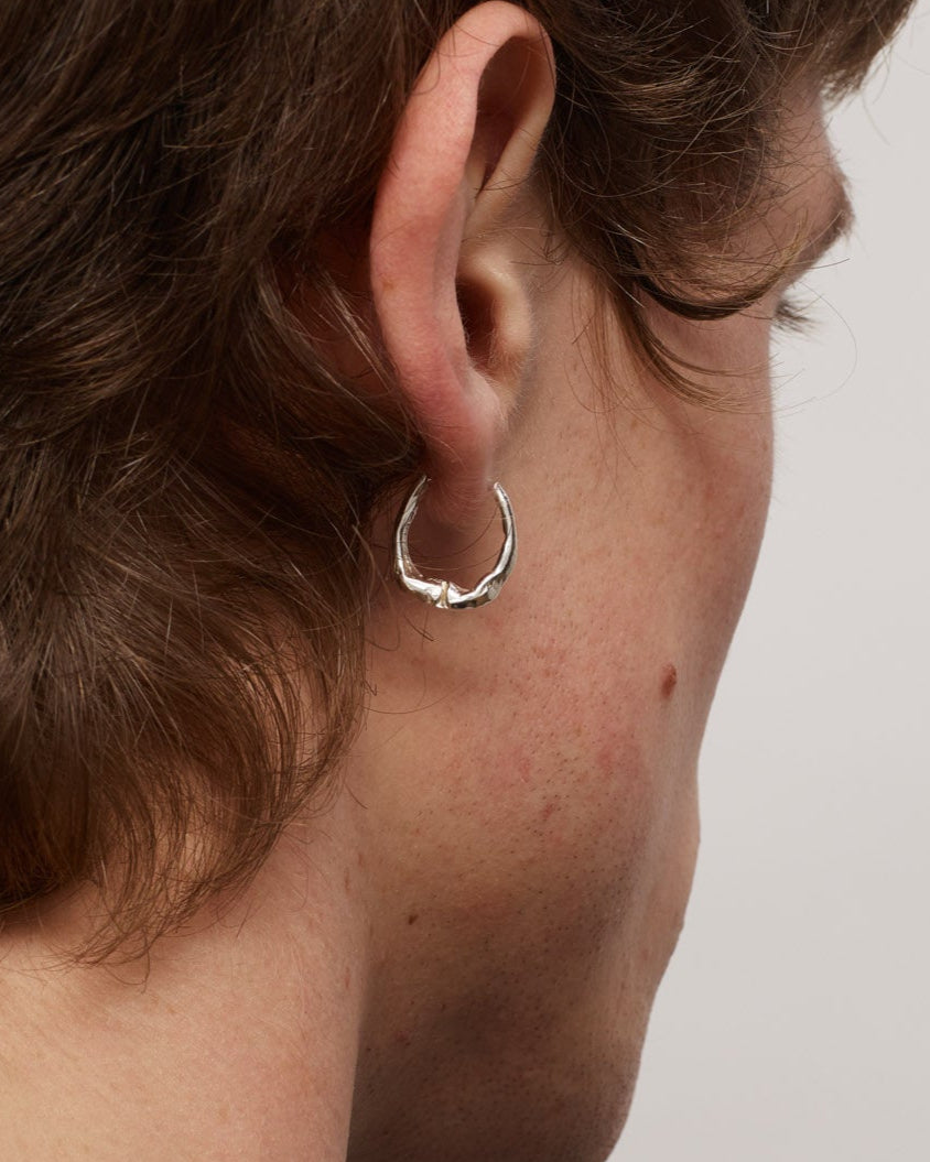 Close-up of a person wearing a silver hoop earring on a neutral background