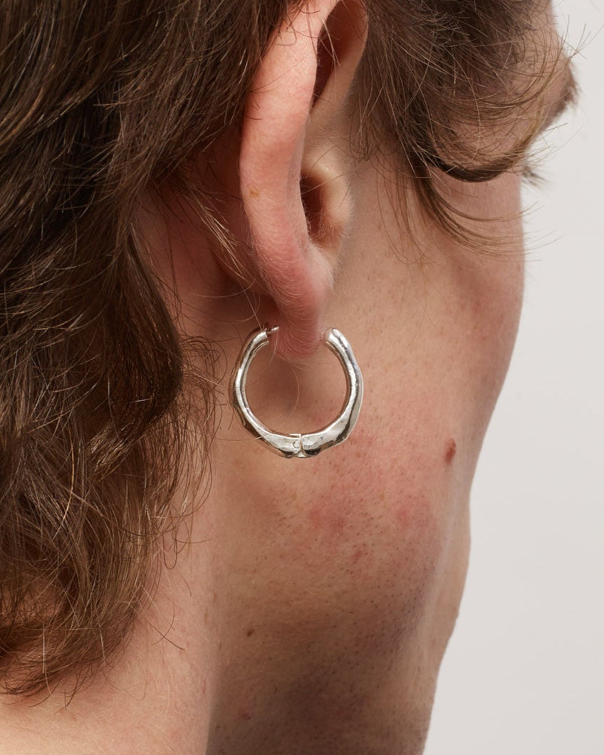Close-up of a person wearing a silver hoop earring on a plain background