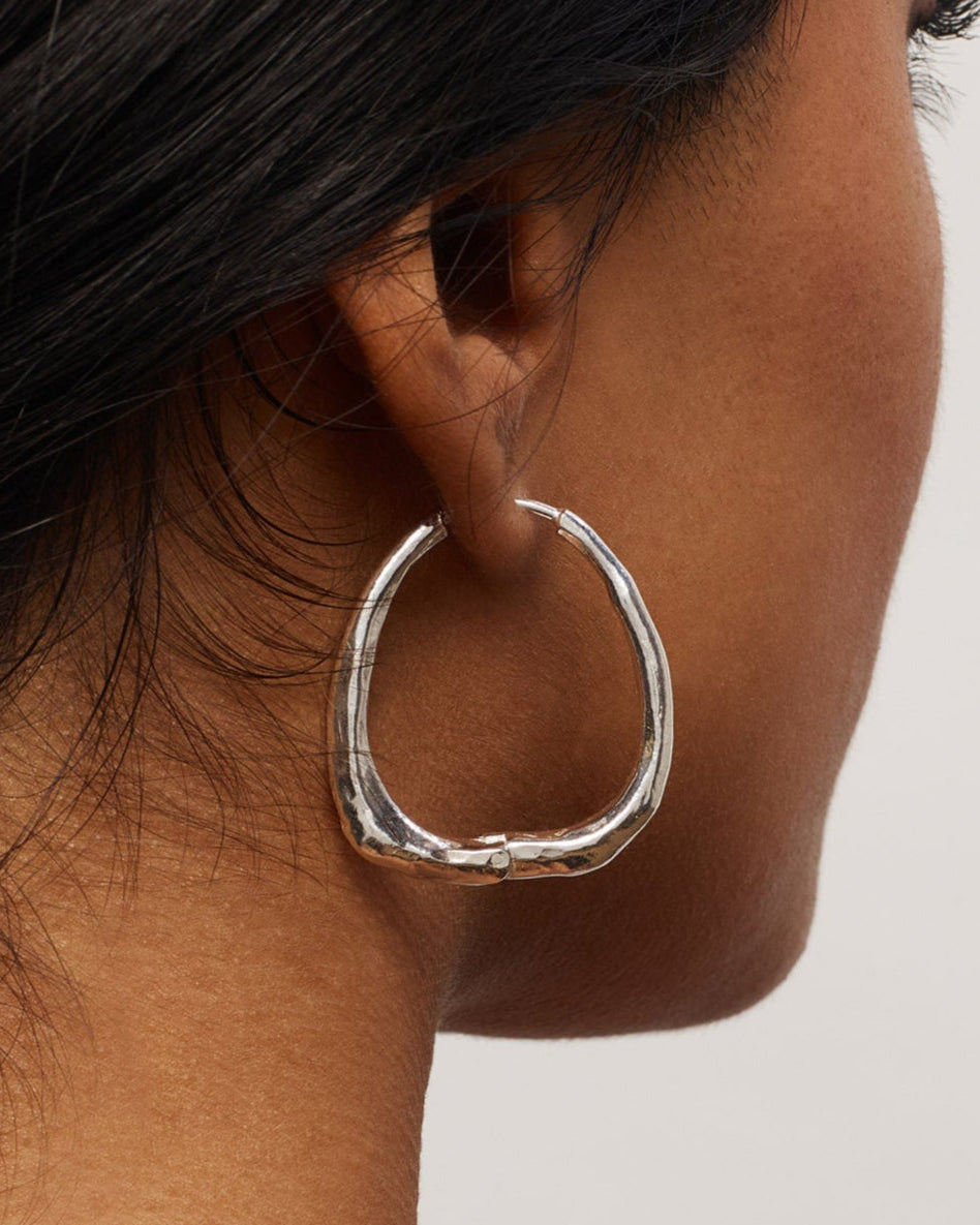 Silver hoop earring worn by a person with a neutral background