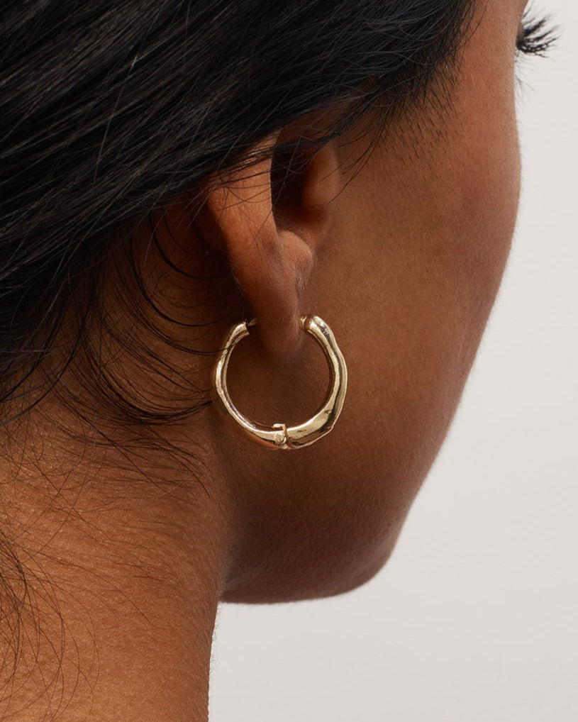 Close-up of a person wearing a gold hoop earring on a plain background