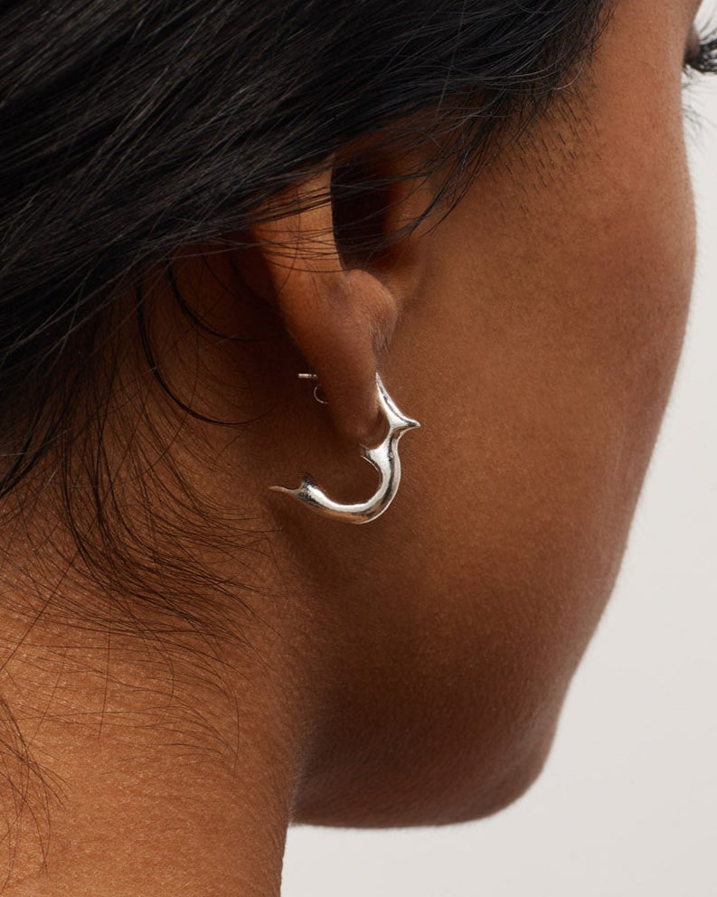 Close-up of a person wearing a silver hoop earring on a neutral background