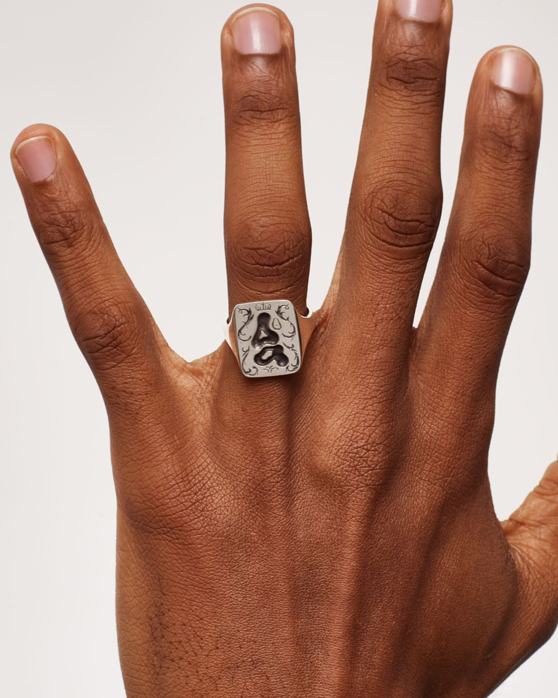 Hand wearing a ring with a visible brand logo on a plain background