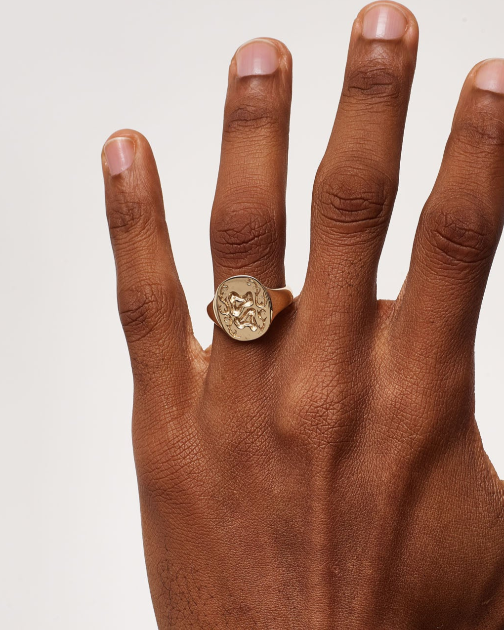 Hand wearing a gold ring on a plain background