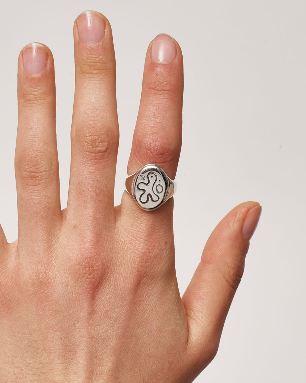 Hand wearing a silver ring with a clover design on a plain background