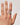 Hand wearing a silver ring with a clover design on a plain background