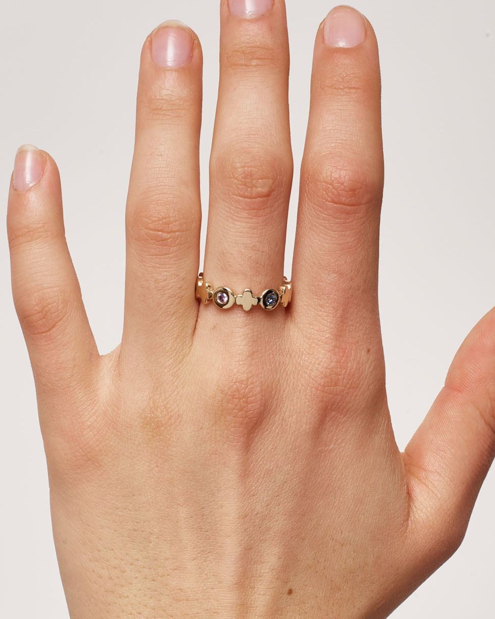 Hand wearing a gold ring with small stones on a plain background
