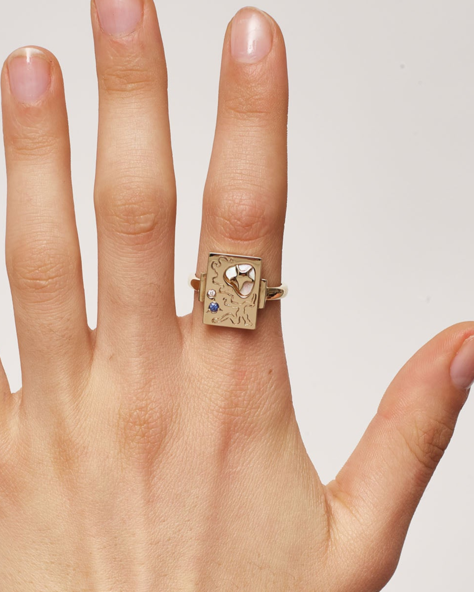 Hand wearing a gold ring with a gemstone on a plain background